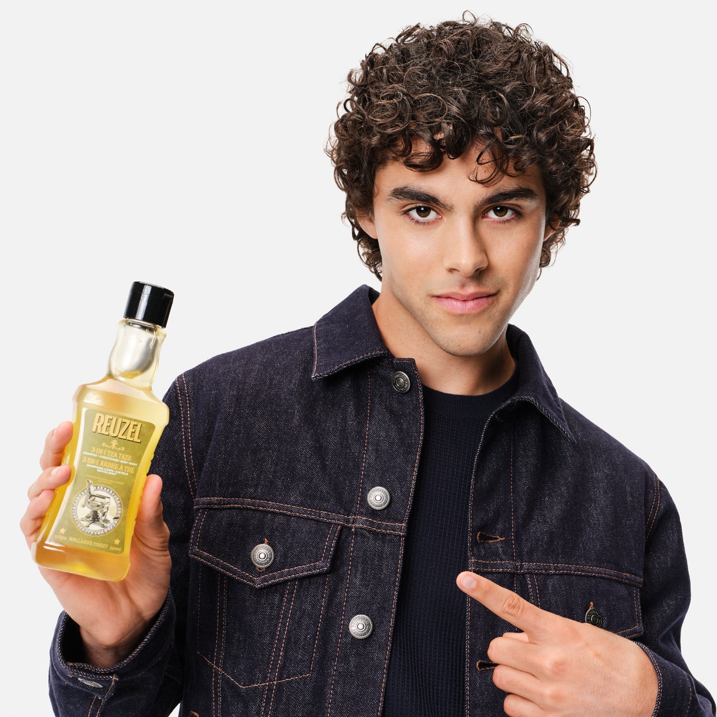 Male model with curly brown hair holding REUZEL 3-in-1 Tea Tree Shampoo