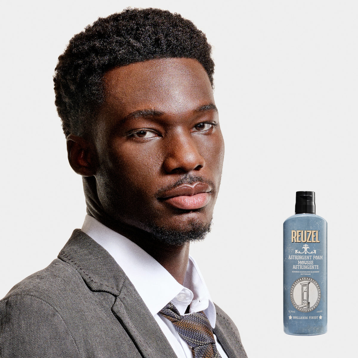 Male model with short textured hair and beard next to REUZEL astringent foam