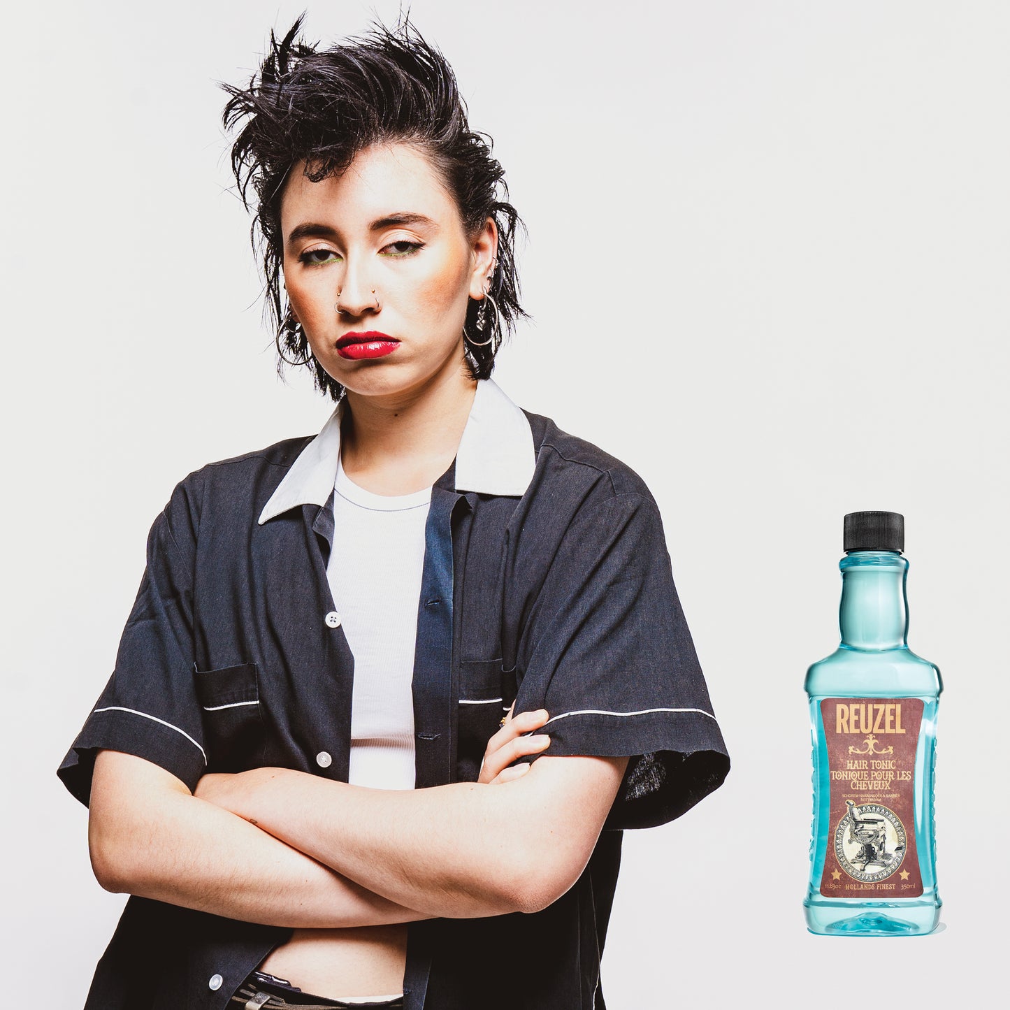 Female model with black spiked up mullet next to REUZEL hair tonic