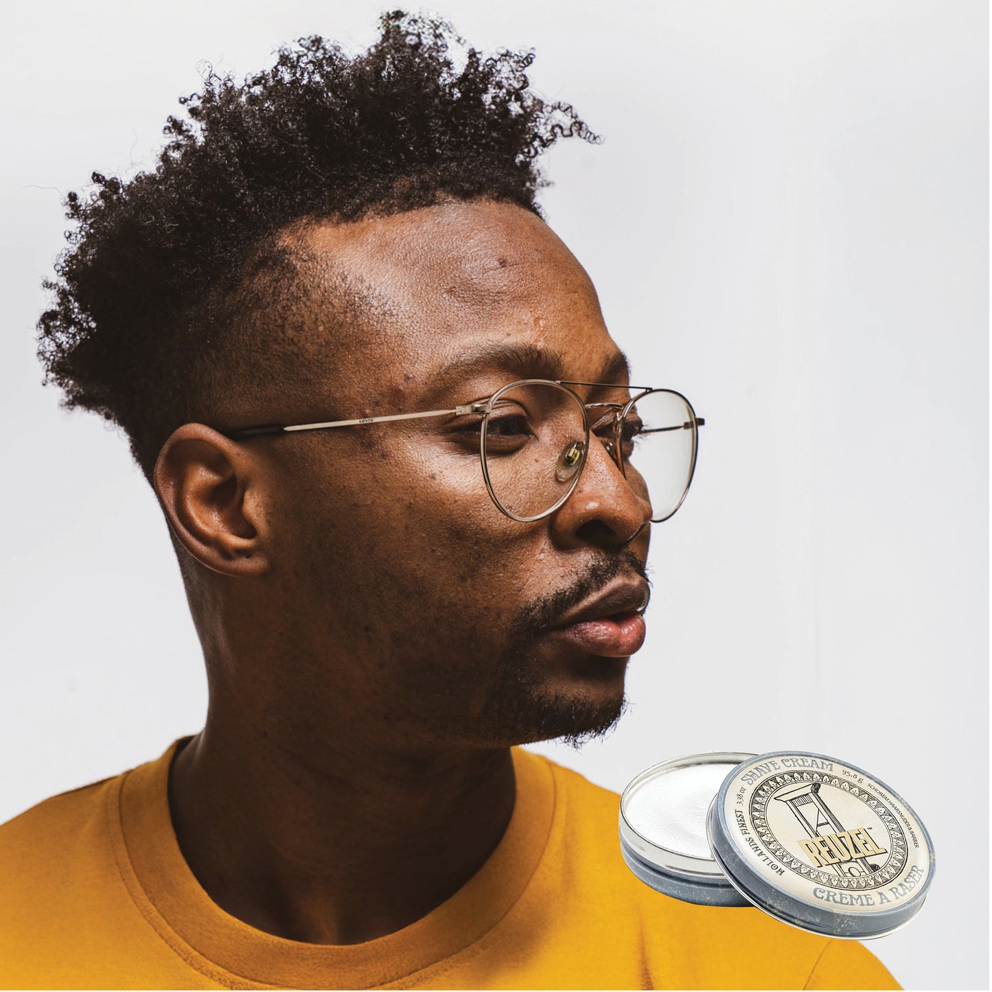 Male model with short black textured hair next to REUZEL shave cream