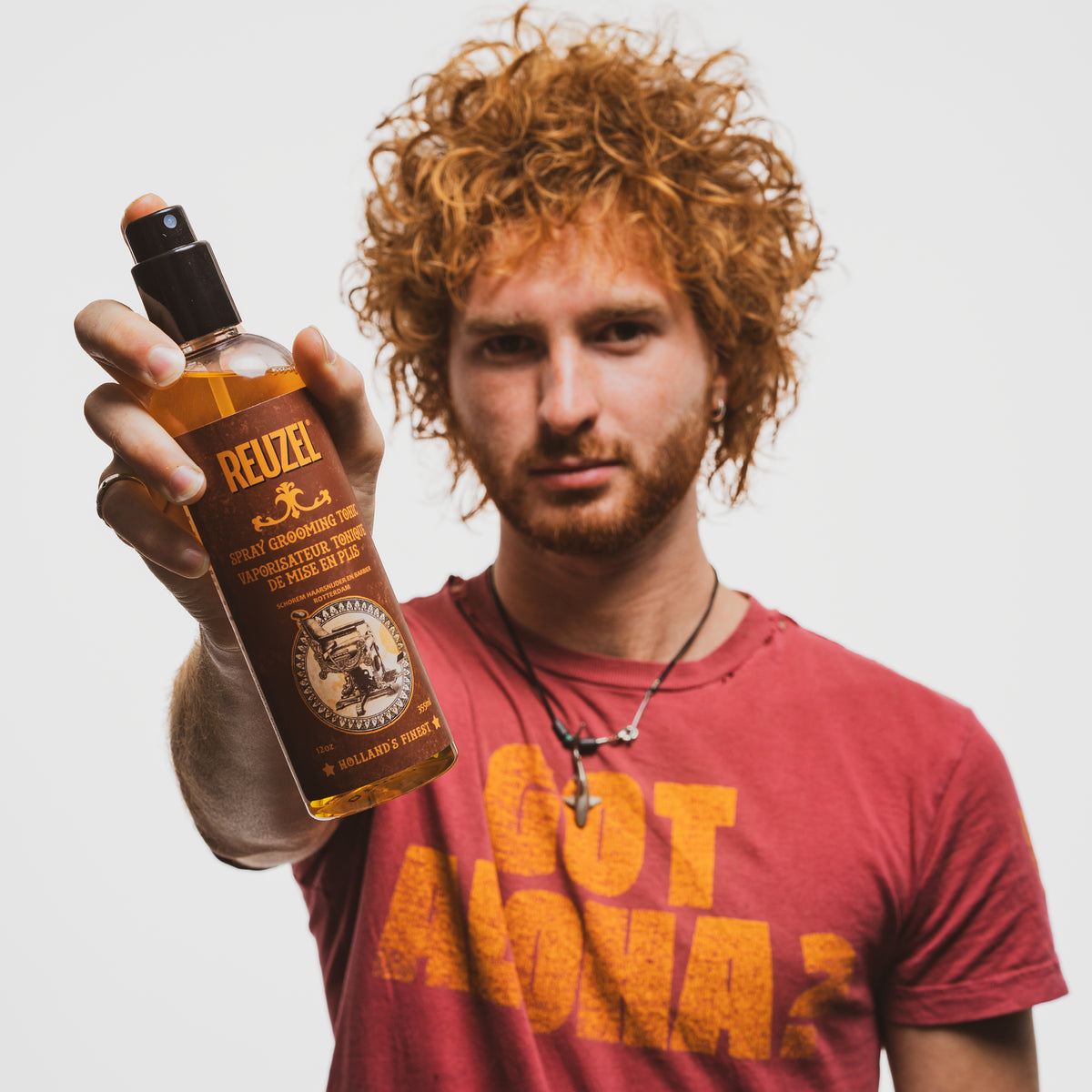 Male model with mid-length textured red hair holding REUZEL spray grooming tonic