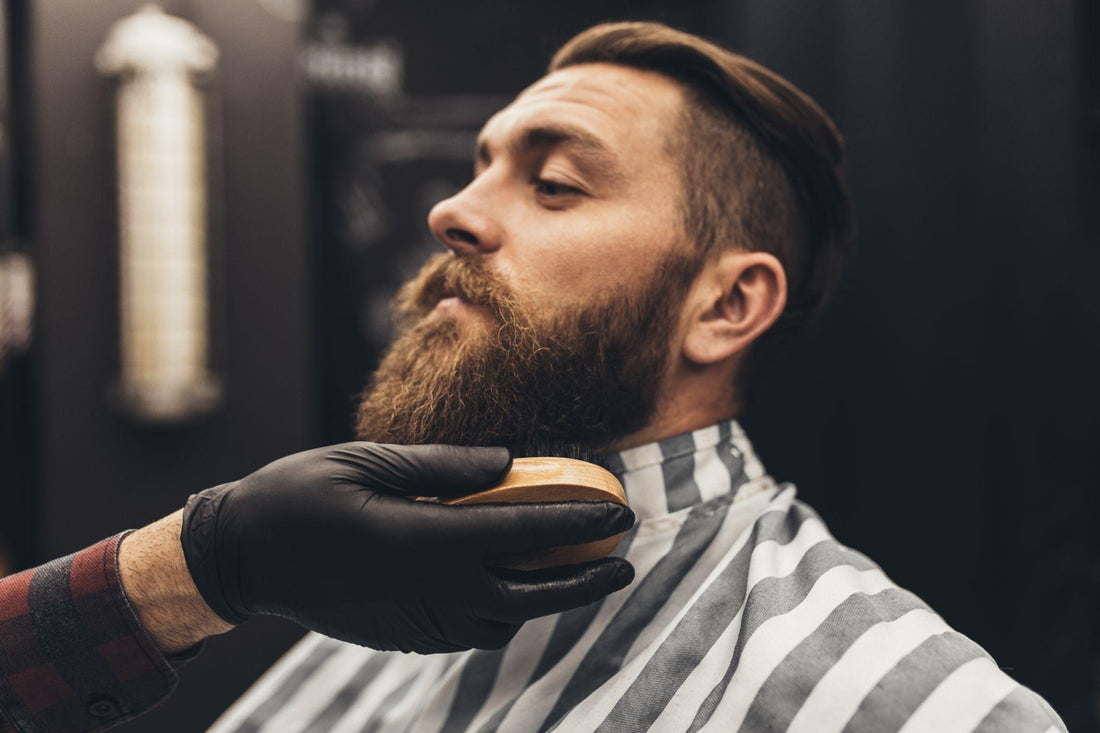 Barber grooming a client’s beard with brush during consultation on hair and product selection