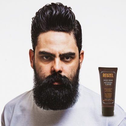 Male model with black hair and full mid-length beard next to REUZEL beard wash