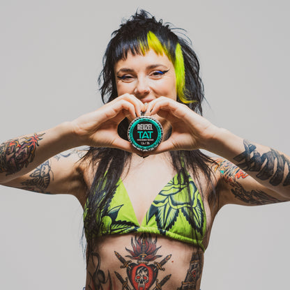 REUZEL TAT Hydrabalm. Image of female model with black and green hair holding hydrabalm 