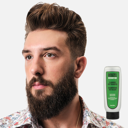 Male model with brown pompadour haircut and beard on white background next to REUZEL FLASHDRY dry shampoo