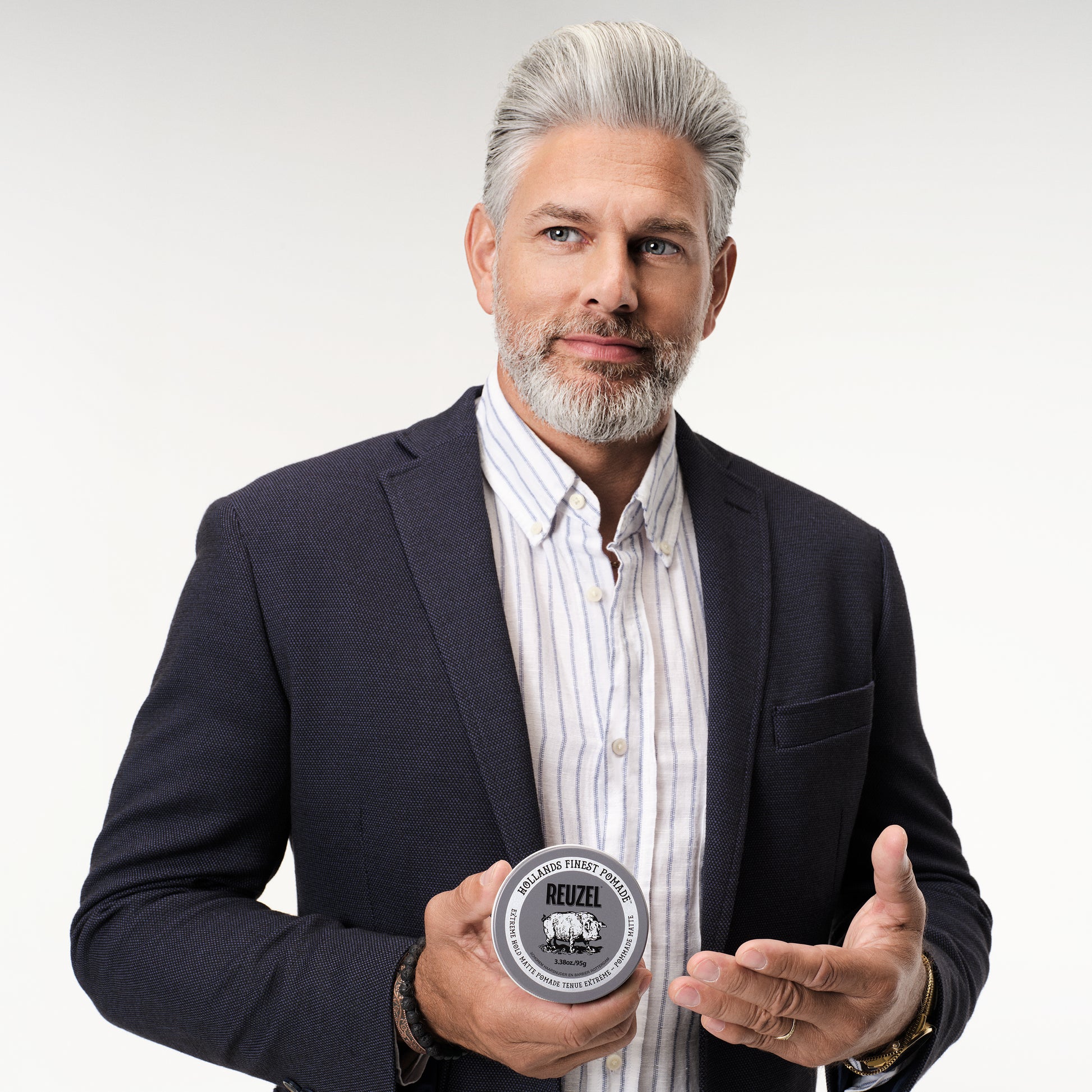 Male model with grey pomadour and beard holding REUZEL extreme matte pomade