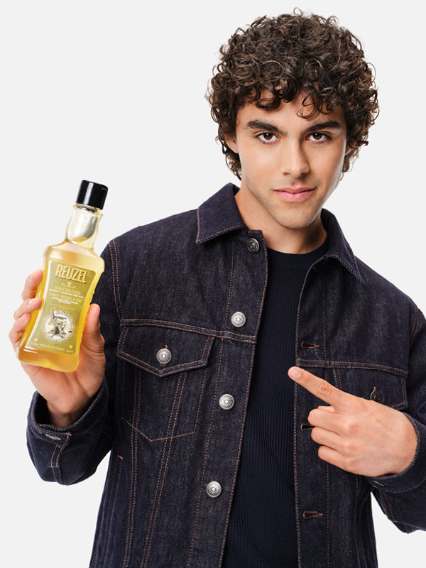 Man with curly hair holding a tin of 3-in-1 Tea Tree Shampoo. Click here to shop Hair, Body, and Skincare products.